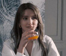 a woman in a white shirt is drinking orange juice from a glass