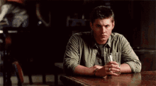 a man is sitting at a table with a glass of whiskey in his hands .