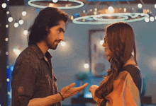 a man and a woman are looking at each other in a room with lights hanging from the ceiling .