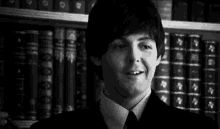 a man in a suit and tie is standing in front of a bookshelf with books .