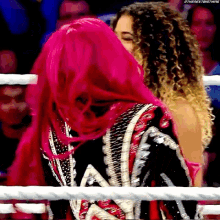 a woman with pink hair is hugging another woman in a wrestling ring