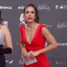 a woman in a red dress is standing on a red carpet holding a piece of paper .