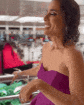 a woman in a purple strapless dress is smiling while holding a shopping cart .