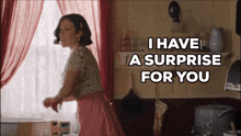 a woman in a pink dress is standing in front of a window and says i have a surprise for you