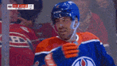 a hockey player wearing a ccm helmet stands in front of a scoreboard