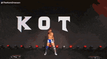 a man without a shirt is standing in front of a large white letter k on a stage .