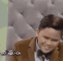 a young man in a suit and bow tie is smiling while sitting on a couch .