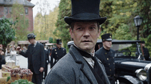 a man wearing a top hat and a suit is standing in front of a crowd of people .