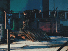 a man in a black jacket is jumping over a wooden plank