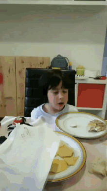 a little girl sits at a table with plates of food