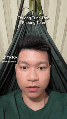 a man in a green shirt is laying in a hammock with the name thương trình tran phương tuấn written on it