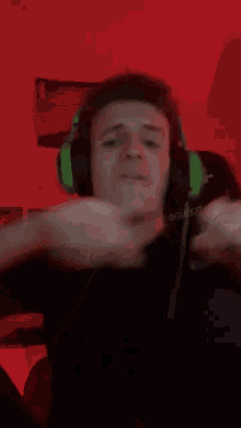 a man wearing green headphones is making a fist in front of a red wall