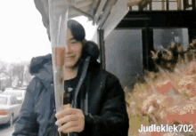 a man in a black jacket is holding a bouquet of flowers with the name judleklek702 on the bottom right