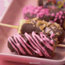 a close up of a chocolate donut with pink icing and the words mr.cakes above it