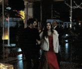 a man in a black suit and a woman in a red dress holding hands