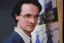 a man in glasses stands in front of a poster for cripsy campson