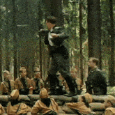 a group of soldiers are gathered in a forest and one of them is standing on a log