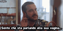 a man with a beard is sitting at a table with the words sento che sta parlando alla sua vagina below him