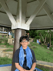 a young man wearing glasses and a blue scarf sitting under a gazebo