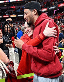 a man in a red hoodie is hugging a woman in a red sweater