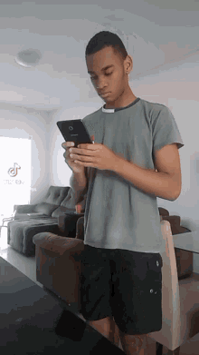 a young man looks at his phone in a living room with a tiktok logo on the wall