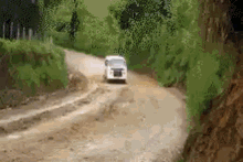 a white van is driving down a dirt road in the woods .