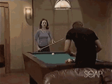 a man and a woman are playing pool in a room with soap on the couch