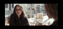 two women are sitting at a table with a cup of coffee
