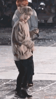 a man in a sweater is dancing on a stage while another man stands behind him .