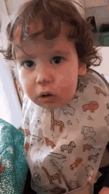 a baby is wearing a bib with animals on it and looking at the camera .