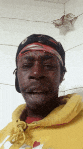 a man wearing a yellow hoodie and a black hat is looking at the camera