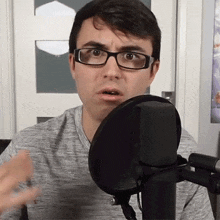 a man wearing glasses is standing in front of a microphone and making a funny face .