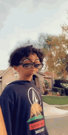 a young boy wearing glasses and a black hoodie is standing on a sidewalk .