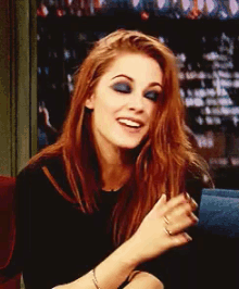 a woman with long red hair is smiling and wearing blue eyeshadow