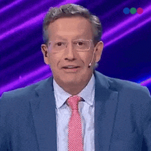 a man in a blue suit and red tie is standing in front of a purple background