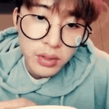 a young man wearing glasses and a blue hoodie is eating a bowl of food .