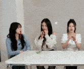 three girls are sitting at a table and one of them is eating a candy