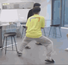 a man in a yellow shirt is standing on one leg in a room with stools .