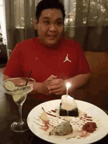 a man in a red shirt is sitting at a table with a martini and a plate of food .