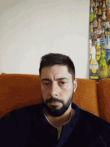 a man with a beard is sitting on a couch in front of a corona beer advertisement