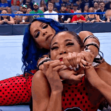 a woman with blue hair is wrestling another woman in front of a crowd