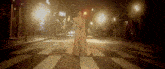 a woman in a long white dress crosses a street at night