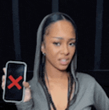a woman in a hoodie is holding a cell phone with a red cross on it .