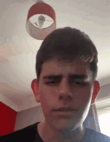 a close up of a young man 's face with a lamp hanging from the ceiling in the background