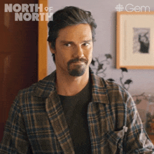 a man in a plaid shirt stands in front of a sign that says north of north on it