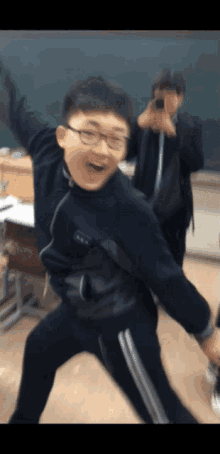 a boy wearing glasses is taking a picture of himself in a classroom