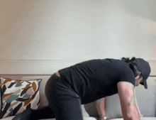 a man wearing a black shirt and a black hat is kneeling on a couch