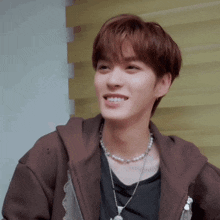 a young man wearing a brown jacket and a pearl necklace