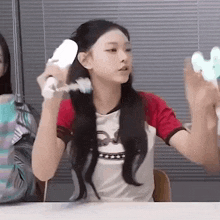a girl is sitting at a table holding a remote control in her hands .