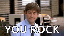 a man in a blue shirt and tie is sitting in front of a sign that says you rock .